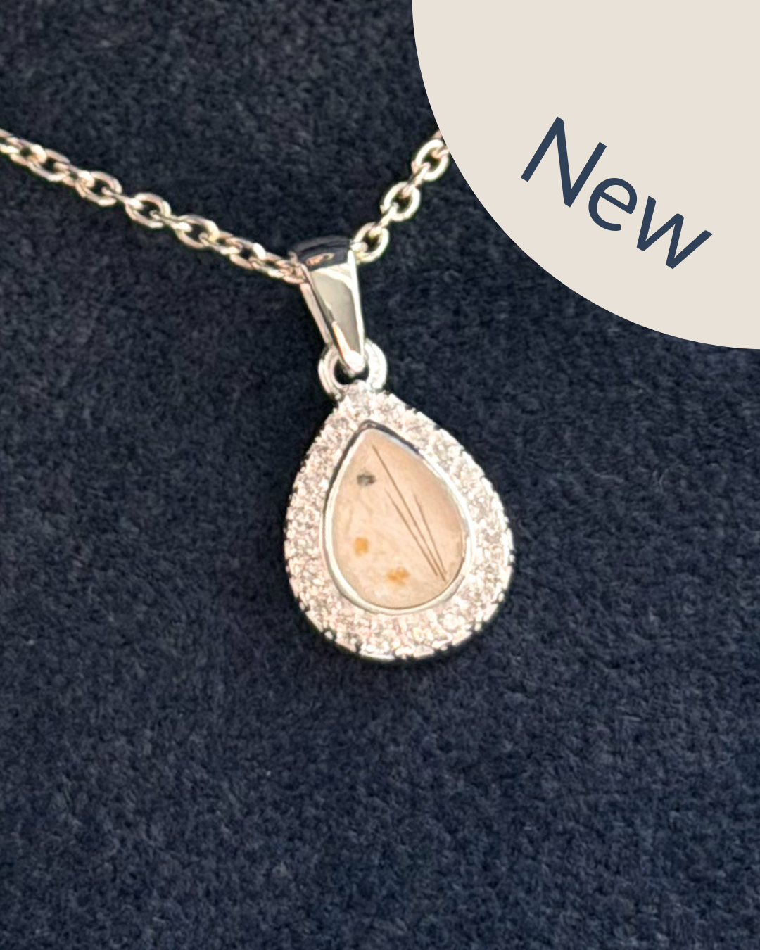 A silver teardrop pendant necklace with a halo of small cubic zirconia stones and a central clear pearl stone containing fine ashes and strands of hair. 