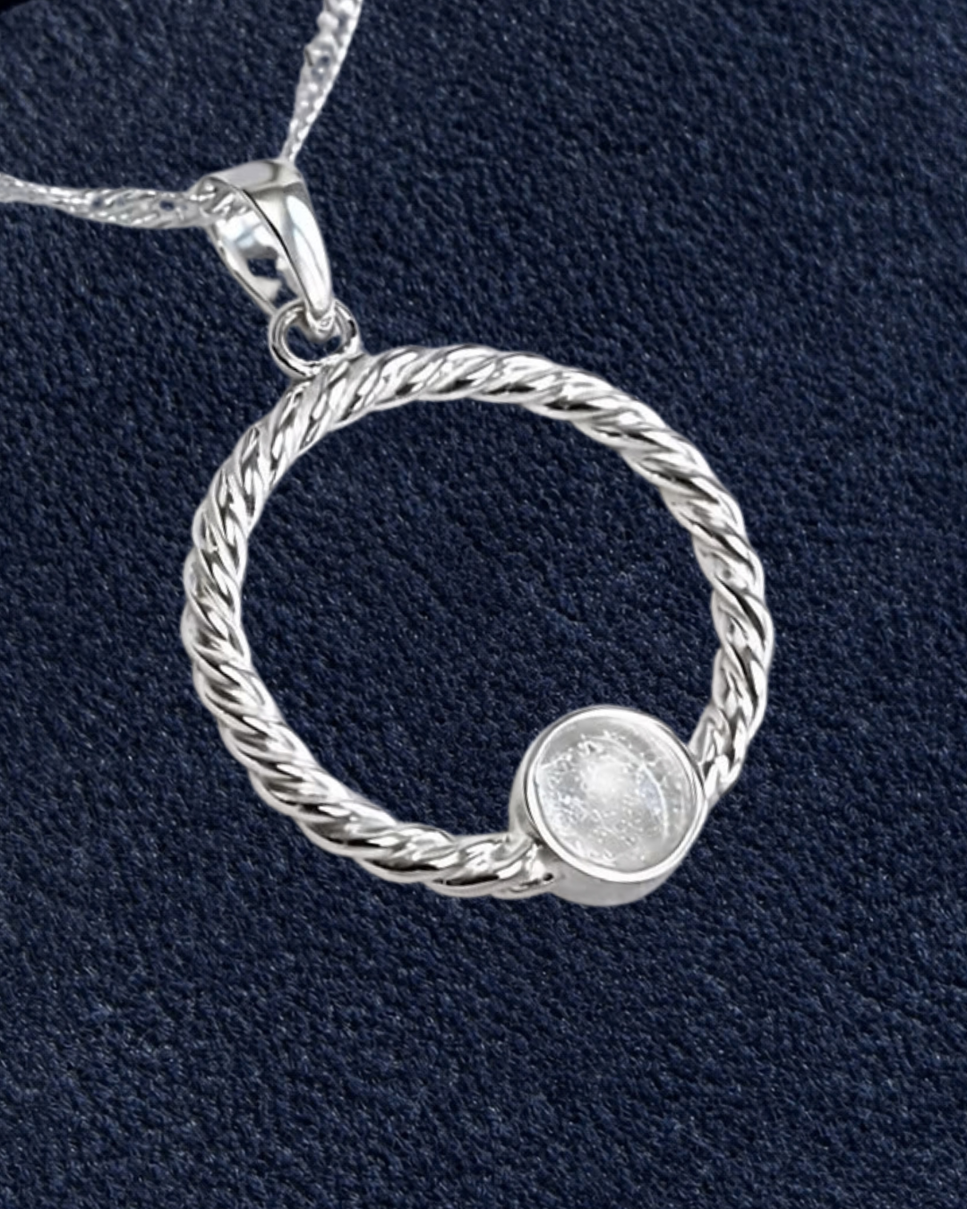A sterling silver twisted rope pendant necklace with a small round bezel-set clear stone, shown on a textured navy blue background with a beige 'New' badge in the top right corner.