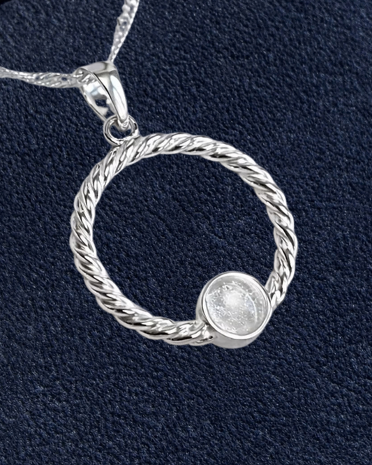 A sterling silver twisted rope pendant necklace with a small round bezel-set clear stone, shown on a textured navy blue background with a beige 'New' badge in the top right corner.