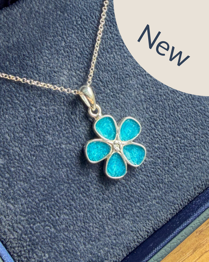 A silver flower-shaped pendant necklace with bright turquoise blue enamel petals, displayed on a textured dark blue velvet surface with a beige 'New' label overlay in the top right corner.