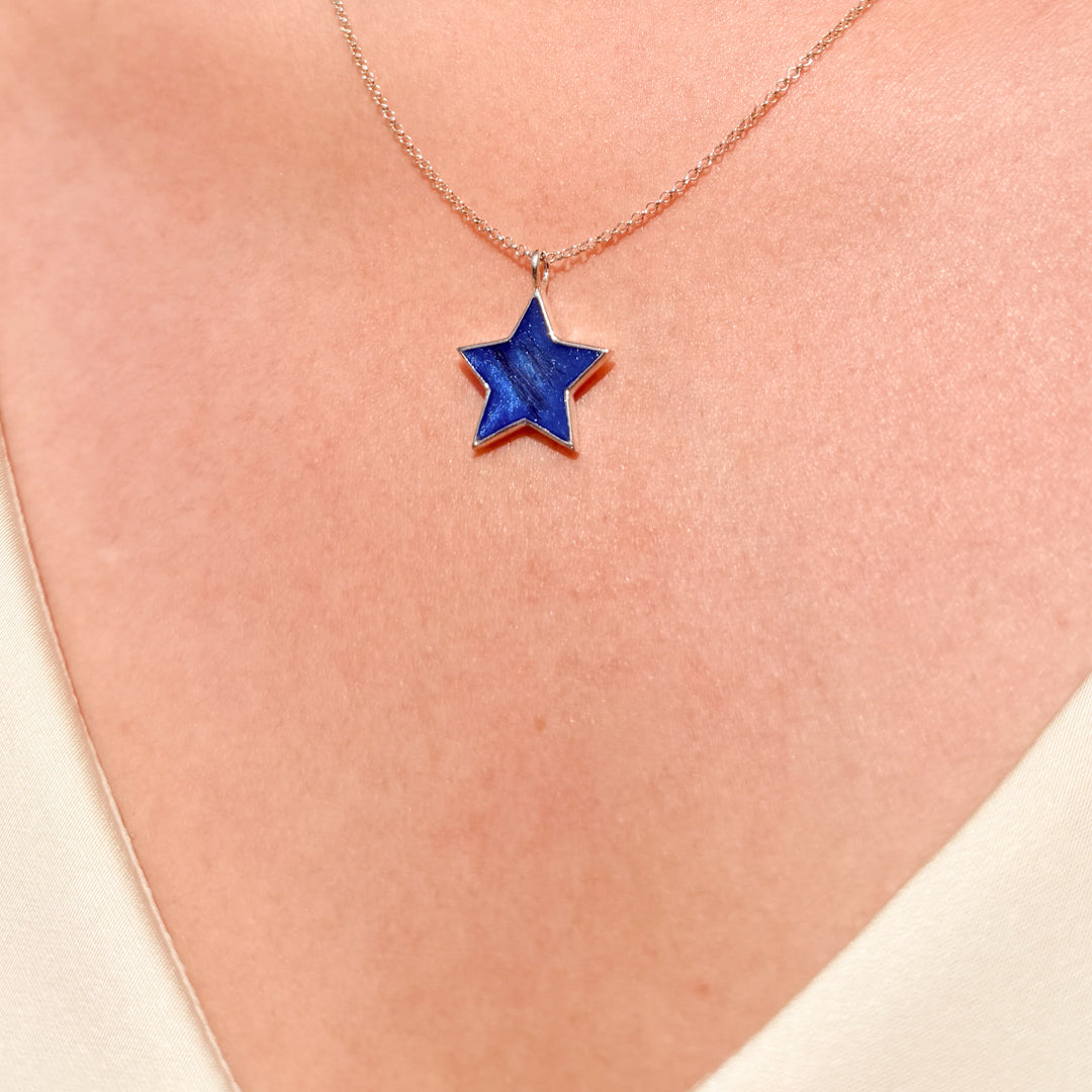A close-up of a person's neck wearing a delicate sterling silver chain necklace with a five-pointed star pendant featuring a deep blue inlay and hair inclusion.
