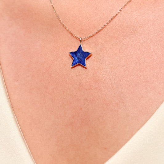 A close-up of a person's neck wearing a delicate sterling silver chain necklace with a five-pointed star pendant featuring a deep blue inlay and hair inclusion.