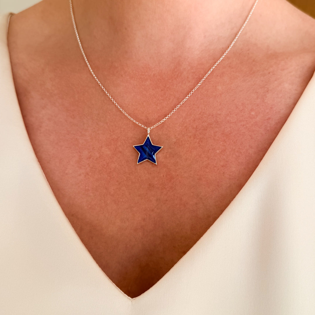 A close-up of a person's neck wearing a delicate sterling silver chain necklace with a five-pointed star pendant featuring a deep blue inlay and hair inclusion.