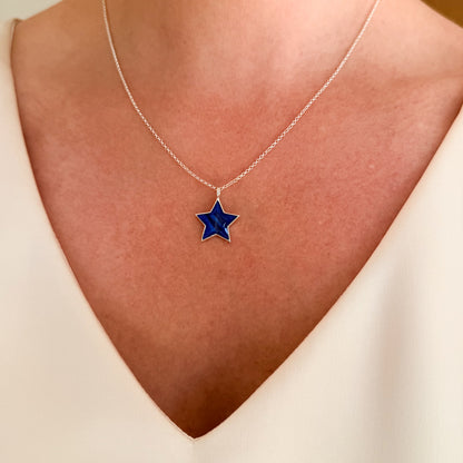 A close-up of a person's neck wearing a delicate sterling silver chain necklace with a five-pointed star pendant featuring a deep blue inlay and hair inclusion.
