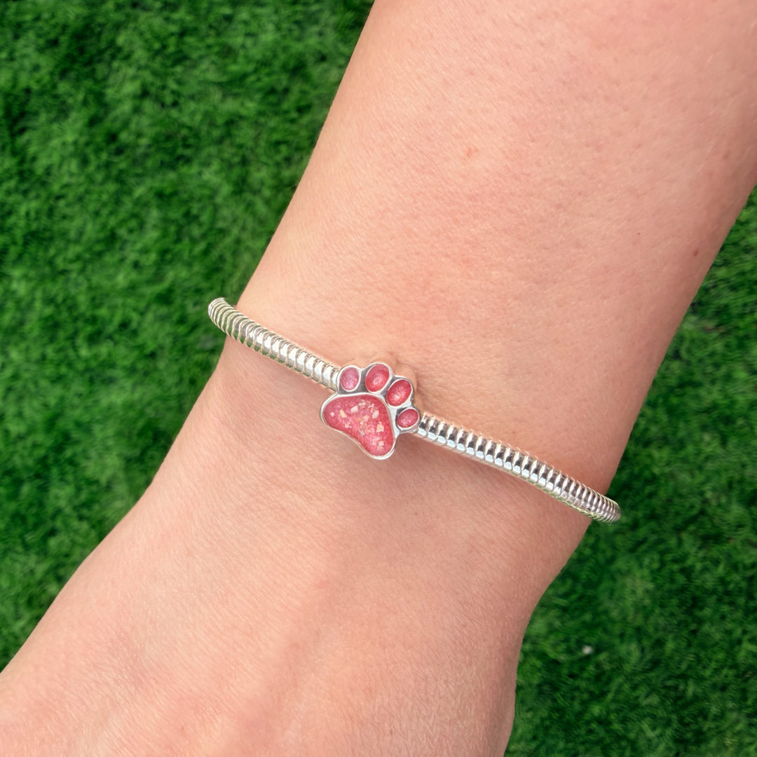 A sterling silver snake chain bracelet featuring a paw print charm filled with textured pink resin and visible inclusions. 