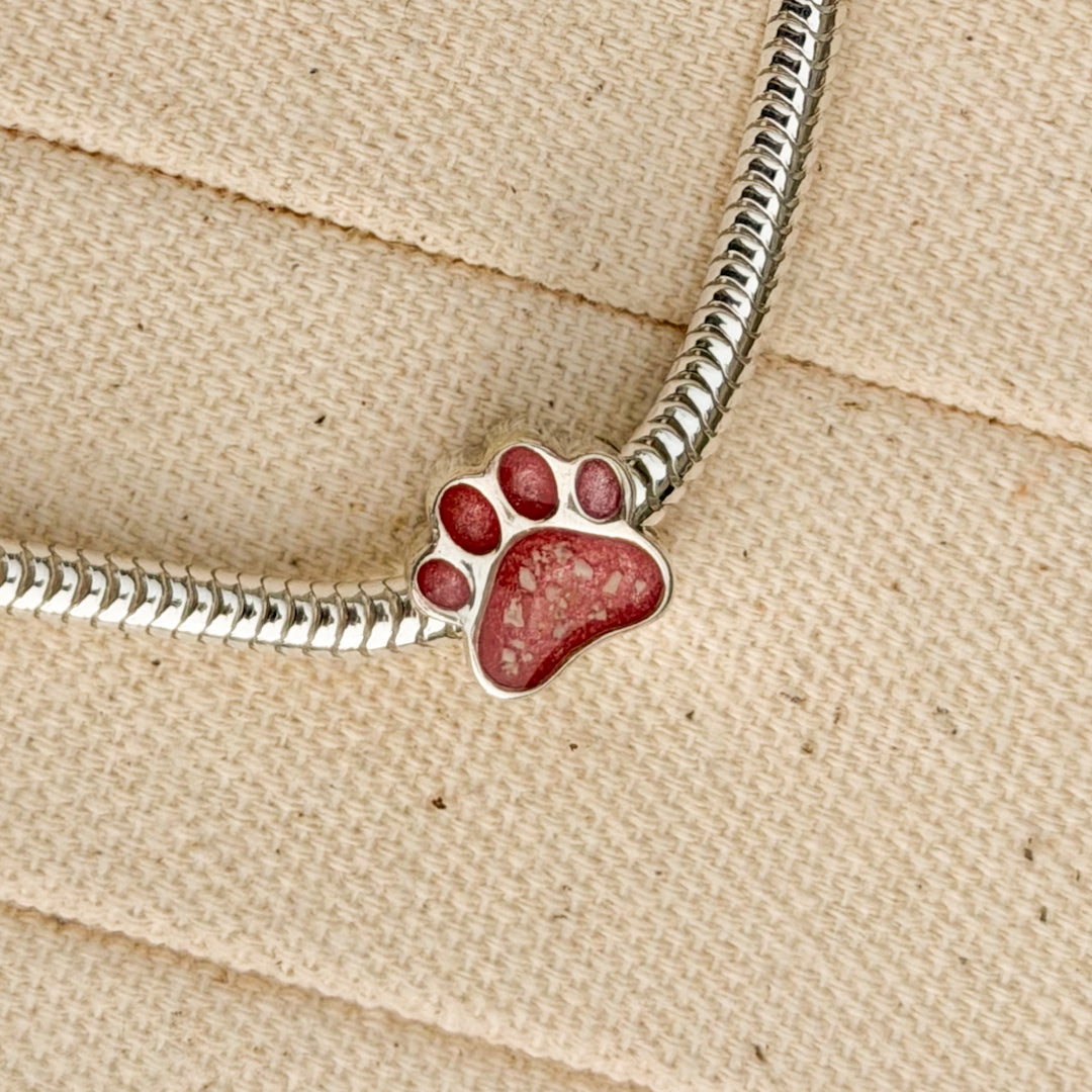 A sterling silver snake chain bracelet featuring a paw print charm filled with textured pink resin and visible inclusions. 