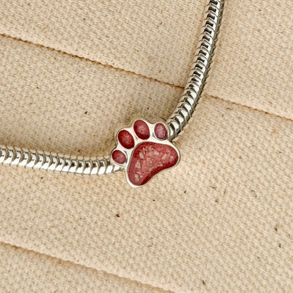 A sterling silver snake chain bracelet featuring a paw print charm filled with textured pink resin and visible inclusions. 