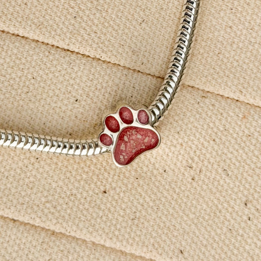 A sterling silver snake chain bracelet featuring a paw print charm filled with textured pink resin and visible inclusions. 