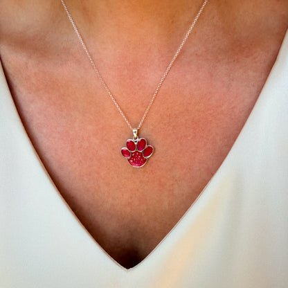 A close-up of a lady wearing a delicate sterling silver chain necklace with a rosey pink paw print pendant with visible ash, styled with a cream V-neck top.