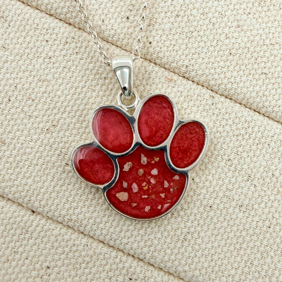 A close-up of sterling silver chain necklace with a rosey pink paw print pendant with visible ash.