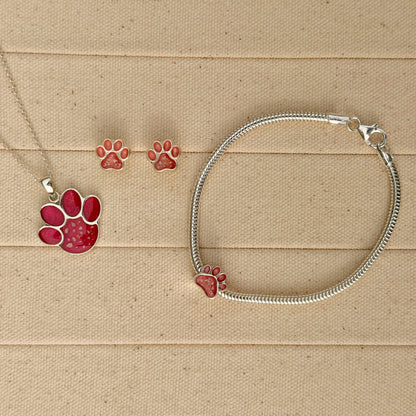 A sterling silver snake chain bracelet with charm, necklace and earrings featuring a paw print filled with textured pink resin and visible inclusions. 