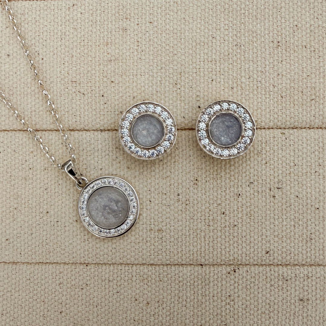 A beautiful set of a matching necklace and earrings in sterling silver surrounded by cubiic zirconia stones with a white silver centre featuring hidden hair inside. 
