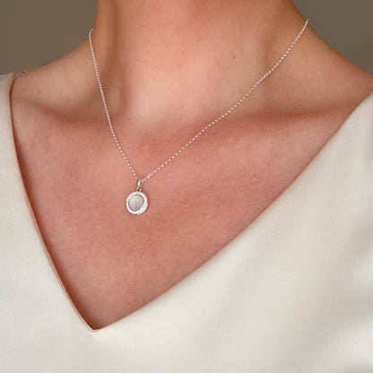 A close-up of a delicate silver chain necklace with a small circular pendant worn on a model's neck, paired with a cream-colored V-neck top.
