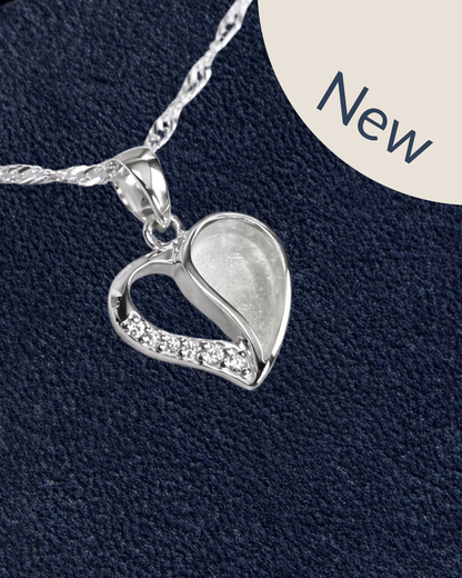 A sterling silver heart-shaped pendant necklace with a small row of clear cubic zirconia stones along one side, shown on a textured dark navy background with a cream circle in the top right containing the word 'New'.