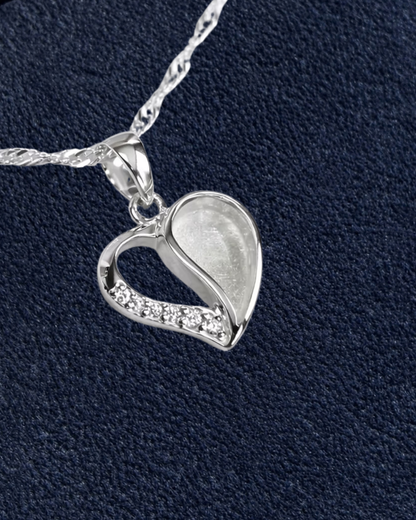 A sterling silver heart-shaped pendant necklace with a small row of clear cubic zirconia stones along one side, shown on a textured dark navy background with a cream circle in the top right containing the word 'New'.