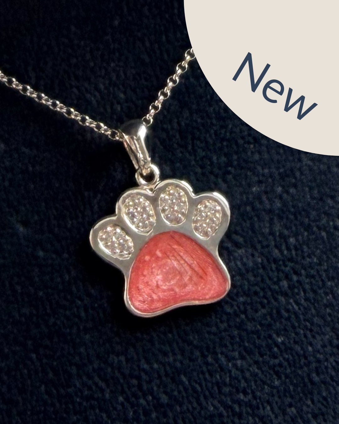 A sterling silver paw print pendant necklace with cubic zirconia with a pink centre with visible hair and ashes.