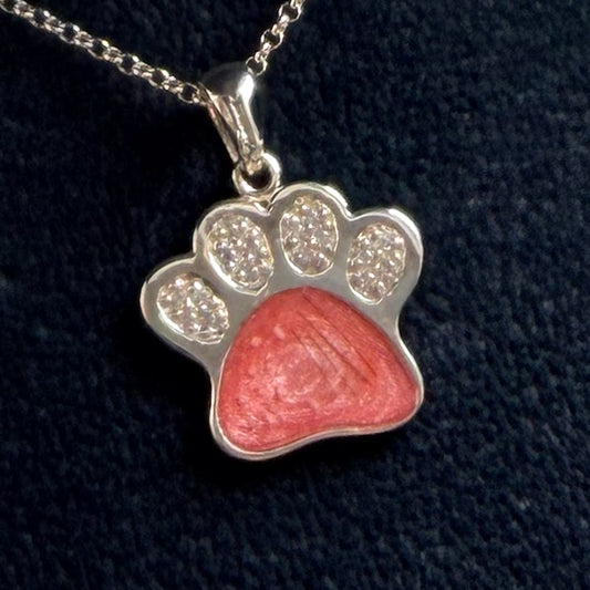 A sterling silver paw print pendant necklace with cubic zirconia with a pink centre with visible hair and ashes.