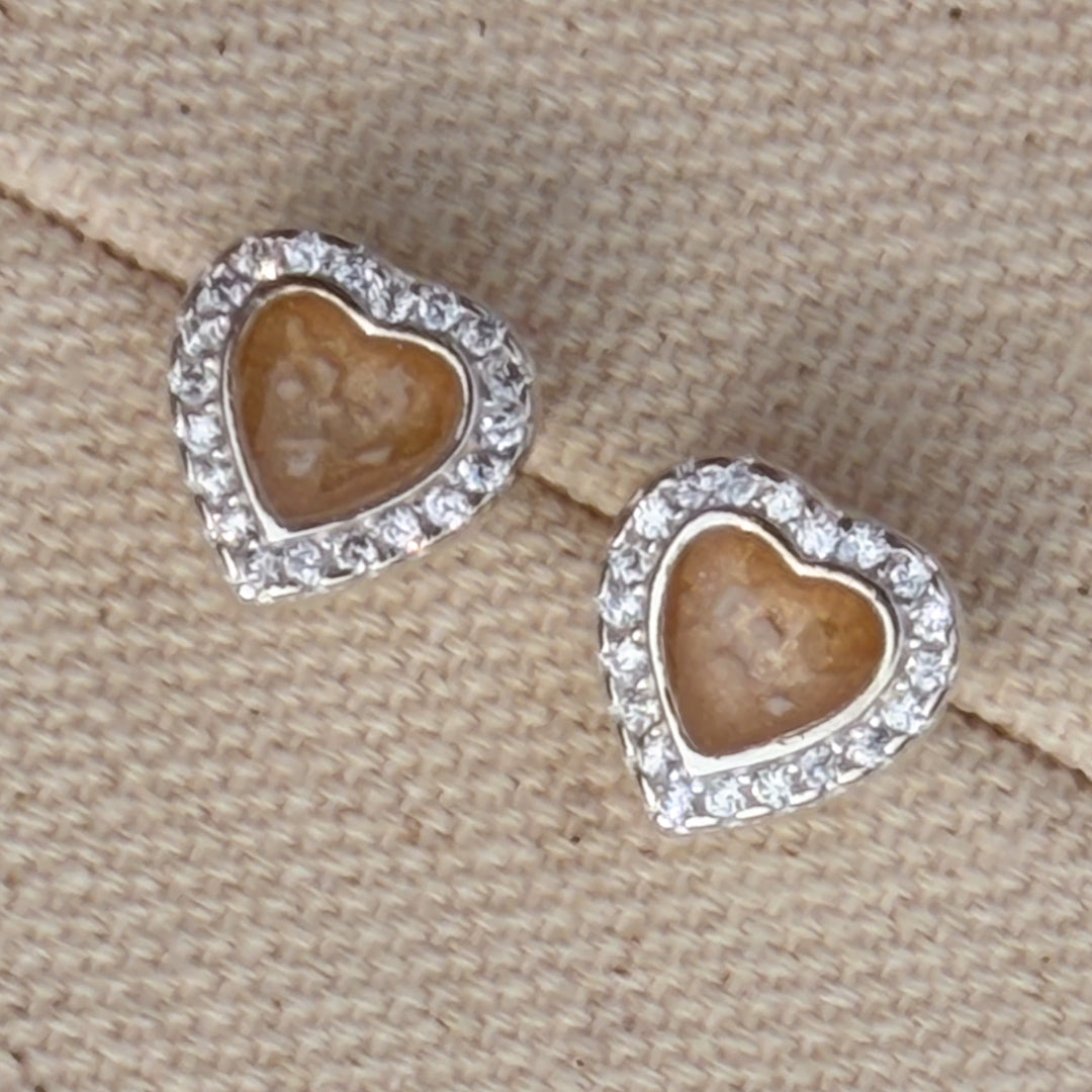 A pair of heart-shaped stud earrings with cubic zirconia borders and champagne centre with visible ash. 