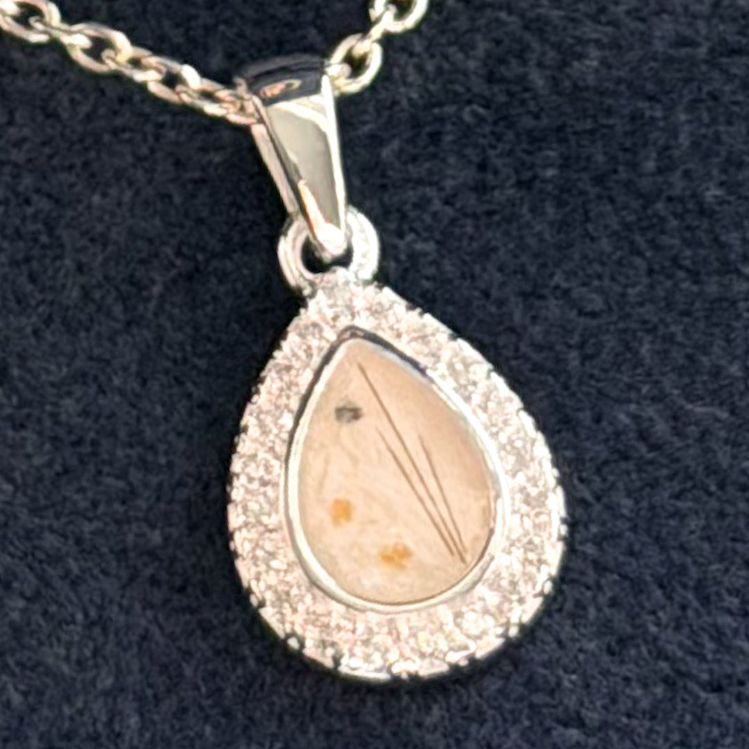 A silver teardrop pendant necklace with a halo of small cubic zirconia stones and a central clear pearl stone containing fine ashes and strands of hair. 