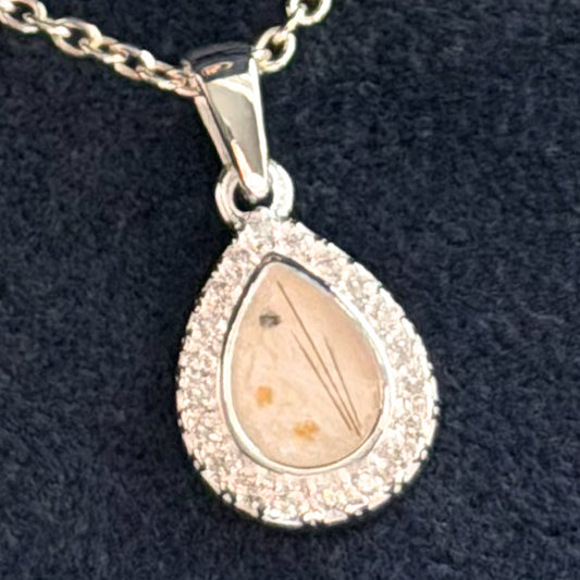 A silver teardrop pendant necklace with a halo of small cubic zirconia stones and a central clear pearl stone containing fine ashes and strands of hair. 